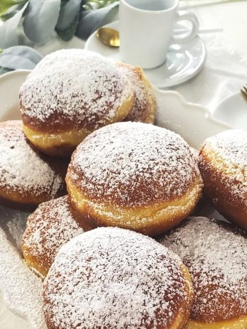 Krapfen on a white serving plate. Coffee cups in the background.